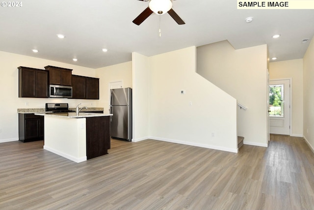 kitchen featuring dark brown cabinetry, stainless steel appliances, a center island with sink, and light hardwood / wood-style flooring