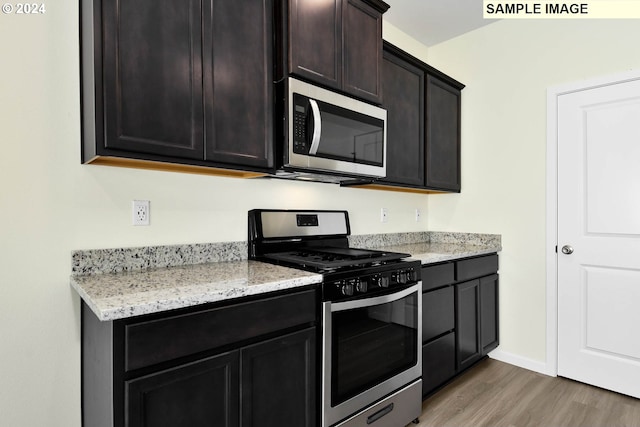 kitchen with light stone countertops, appliances with stainless steel finishes, dark brown cabinets, and light hardwood / wood-style flooring