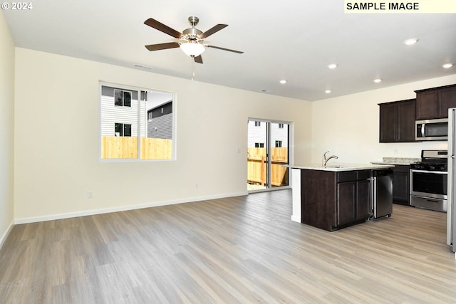 kitchen featuring light hardwood / wood-style flooring, dark brown cabinets, stainless steel appliances, light stone countertops, and a center island with sink