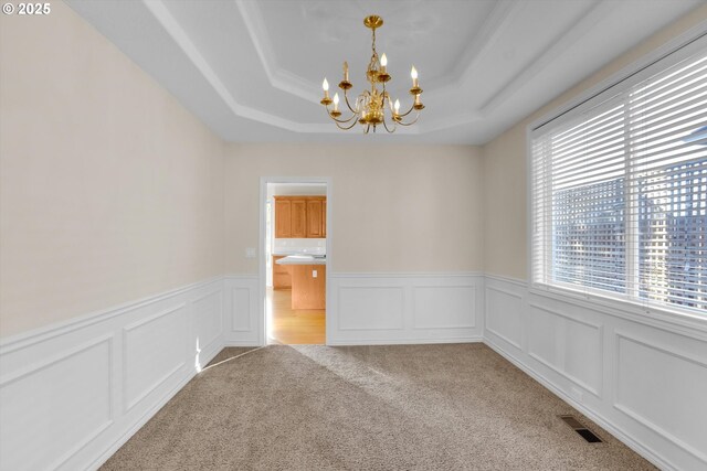 unfurnished room with visible vents, an inviting chandelier, a raised ceiling, a decorative wall, and light colored carpet