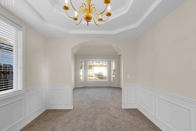 unfurnished room featuring arched walkways, a raised ceiling, an inviting chandelier, and wainscoting