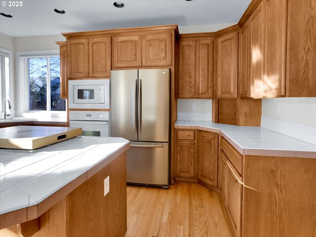 kitchen featuring tile countertops, brown cabinets, light wood-style floors, white appliances, and a sink