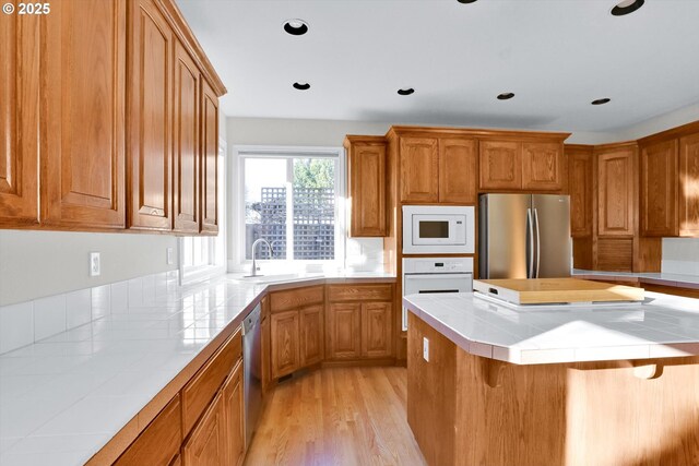 kitchen with brown cabinetry, a sink, appliances with stainless steel finishes, and tile counters