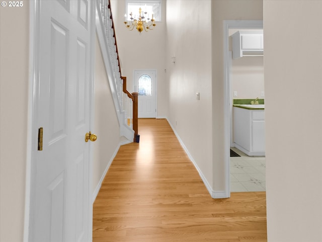 foyer with light wood-type flooring, baseboards, an inviting chandelier, and stairs