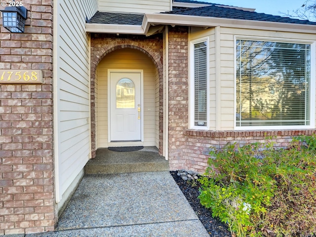 property entrance featuring brick siding and roof with shingles