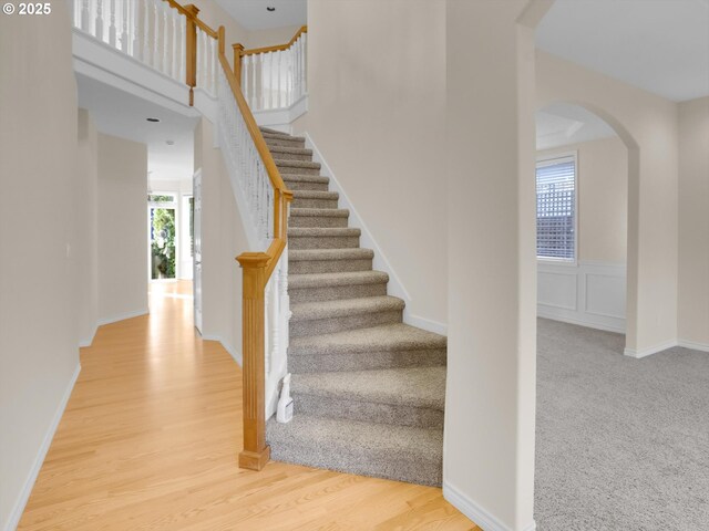 staircase featuring wood finished floors, a wainscoted wall, baseboards, arched walkways, and a towering ceiling