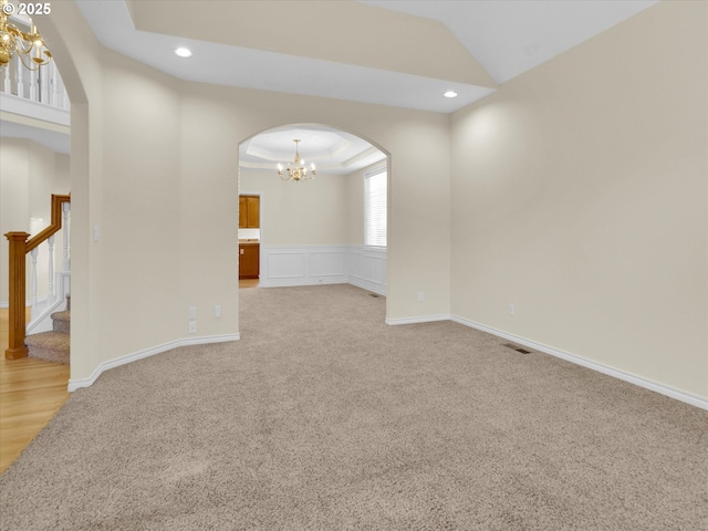 spare room with a tray ceiling, recessed lighting, arched walkways, stairs, and a notable chandelier