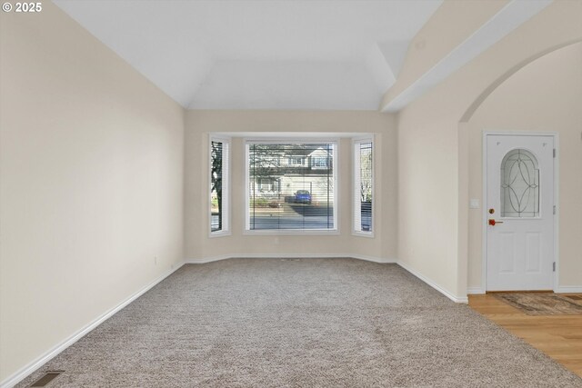 foyer entrance featuring baseboards, visible vents, light wood-style flooring, arched walkways, and vaulted ceiling