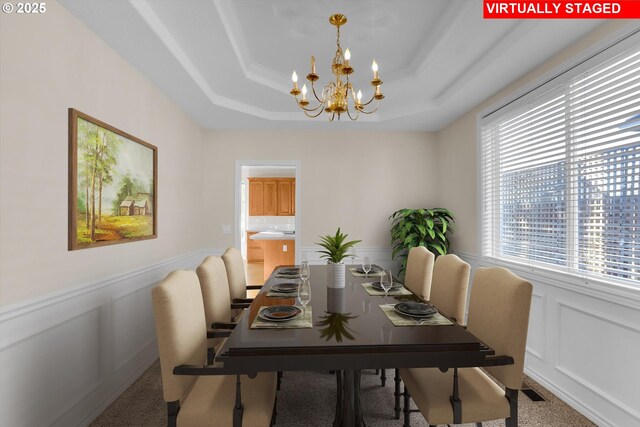 dining space featuring a decorative wall, a raised ceiling, an inviting chandelier, and a wainscoted wall