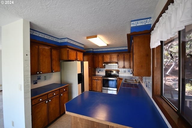 kitchen with sink, stainless steel range with electric cooktop, decorative backsplash, white fridge with ice dispenser, and a textured ceiling