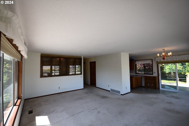 spare room featuring a textured ceiling, a wealth of natural light, a chandelier, and carpet flooring