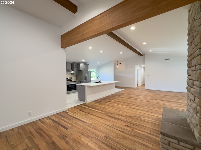 unfurnished living room with light hardwood / wood-style floors, lofted ceiling with beams, and sink