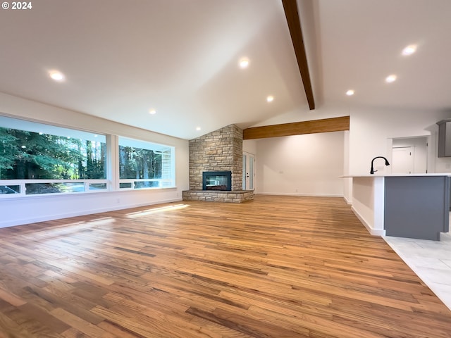 unfurnished living room featuring a fireplace, light hardwood / wood-style flooring, and lofted ceiling with beams