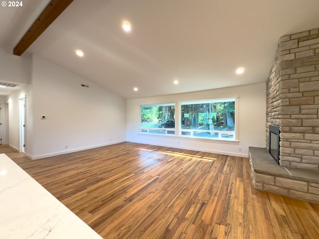 unfurnished living room with a stone fireplace, lofted ceiling with beams, and wood-type flooring