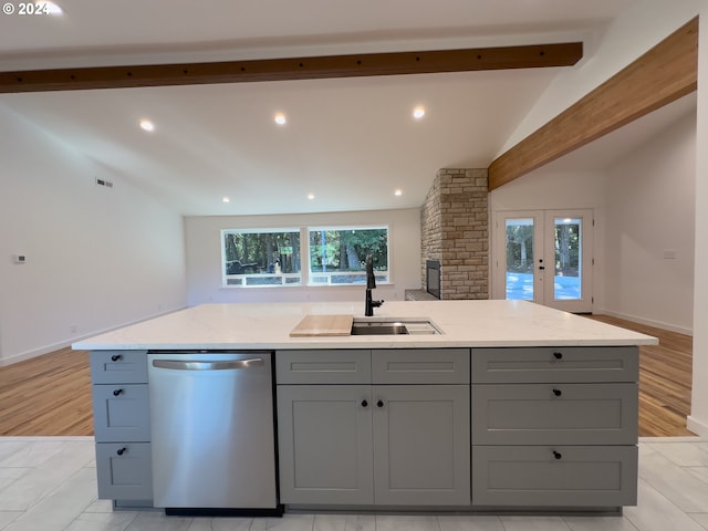 kitchen with light wood-type flooring, vaulted ceiling with beams, a center island with sink, and dishwasher