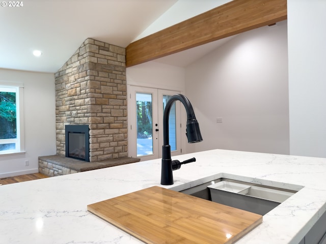 interior space featuring a stone fireplace, hardwood / wood-style floors, light stone countertops, sink, and lofted ceiling with beams