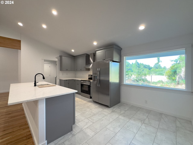 kitchen with wall chimney range hood, light wood-type flooring, gray cabinets, appliances with stainless steel finishes, and sink