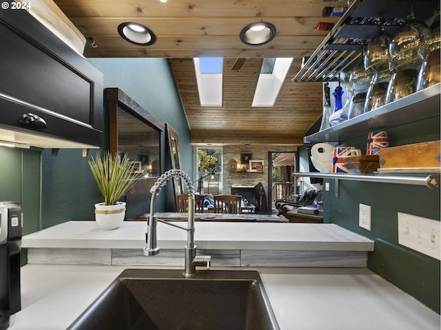 kitchen with sink, vaulted ceiling with skylight, a stone fireplace, and wood ceiling