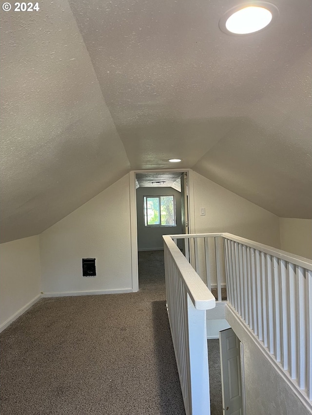 additional living space with lofted ceiling, a textured ceiling, and dark colored carpet