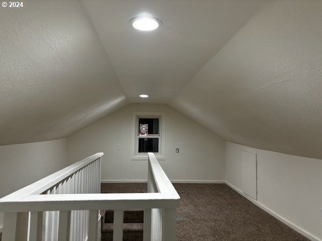 additional living space featuring vaulted ceiling and dark colored carpet