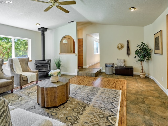 living room featuring lofted ceiling, a wood stove, ceiling fan, and a textured ceiling