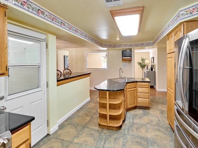 kitchen with light brown cabinetry, stainless steel fridge, sink, and a kitchen island