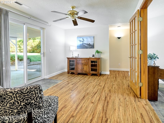 living room with a textured ceiling, ceiling fan, and light hardwood / wood-style flooring