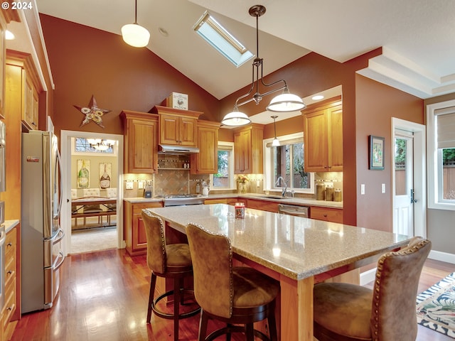 kitchen featuring decorative light fixtures, backsplash, a skylight, a kitchen island, and stainless steel appliances