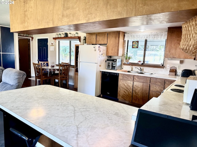 kitchen featuring a sink, light countertops, freestanding refrigerator, brown cabinets, and dishwasher