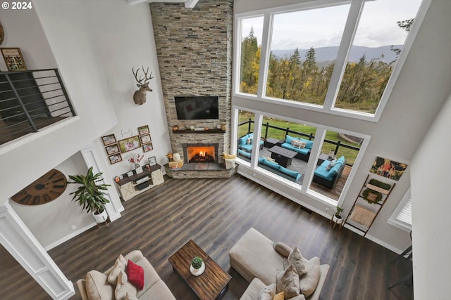 living room featuring a stone fireplace, dark wood-type flooring, and a high ceiling