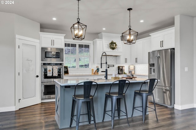 kitchen featuring white cabinetry, stainless steel appliances, pendant lighting, and an island with sink