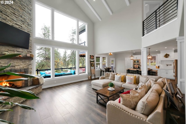 living room with a stone fireplace, ornate columns, dark hardwood / wood-style floors, high vaulted ceiling, and beam ceiling