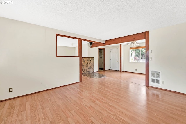 empty room featuring a textured ceiling, light wood-type flooring, ceiling fan, and heating unit