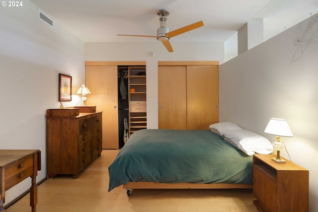 bedroom featuring light hardwood / wood-style floors, ceiling fan, and multiple closets