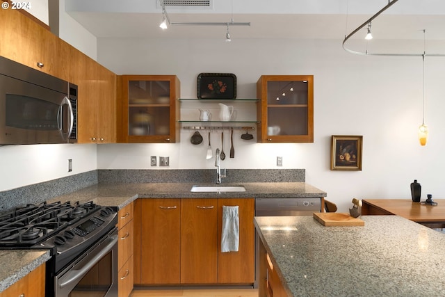 kitchen with rail lighting, stainless steel appliances, dark stone countertops, and sink