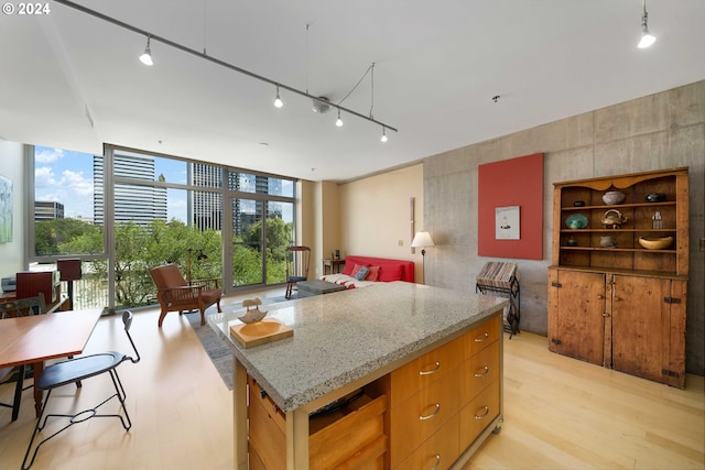 kitchen featuring light stone countertops, track lighting, light hardwood / wood-style flooring, and a wall of windows