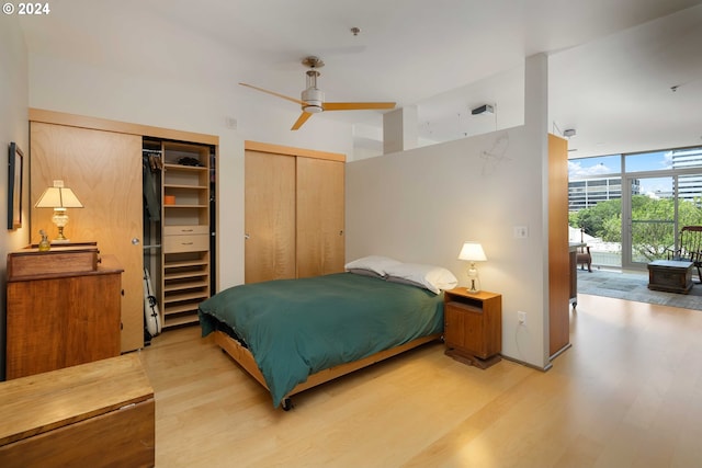 bedroom with hardwood / wood-style floors, a wall of windows, ceiling fan, and multiple closets