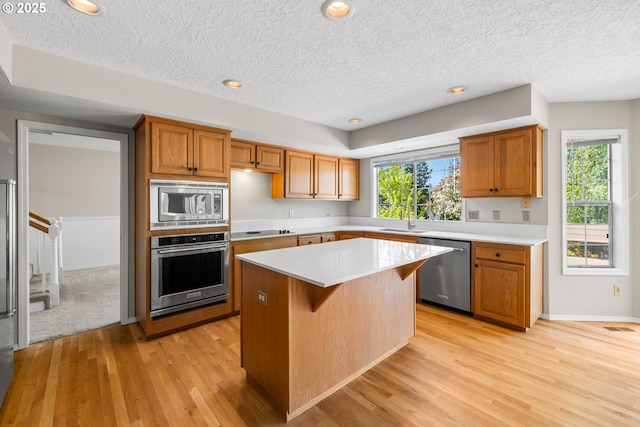 5393 SW Wichita St, Tualatin, OR 97062 - kitchen featuring appliances with stainless steel finishes, light wood-style flooring, light countertops, a textured ceiling, and a center island