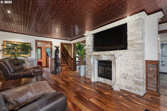 living room featuring a stone fireplace, ornamental molding, and dark hardwood / wood-style flooring