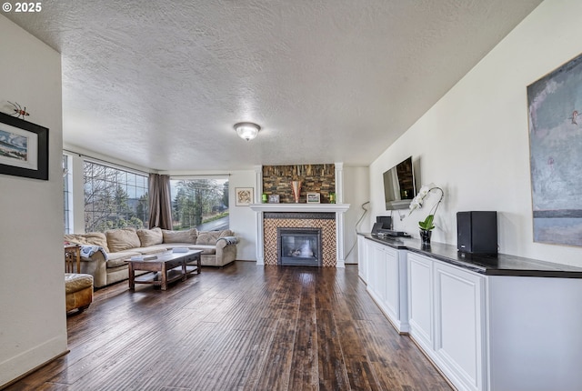 living room featuring a textured ceiling, dark wood-type flooring, and a tiled fireplace