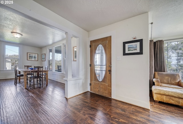 foyer entrance with dark wood-style flooring, a healthy amount of sunlight, and decorative columns