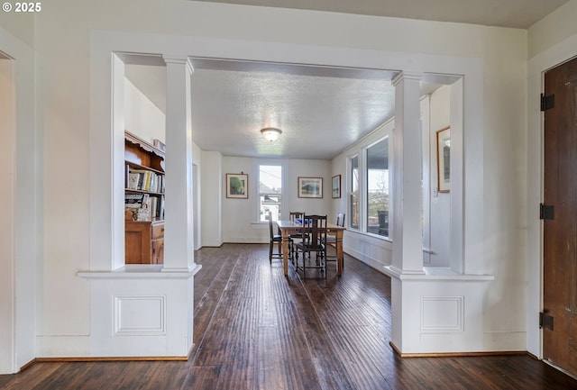 dining area with decorative columns, baseboards, wood-type flooring, and a textured ceiling