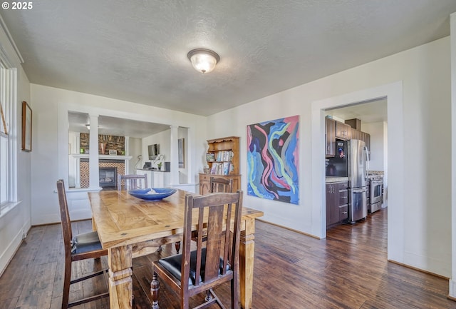 dining space with a large fireplace, dark wood-type flooring, a textured ceiling, and baseboards