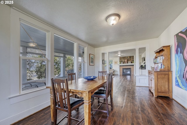 dining area with a textured ceiling, dark wood-style flooring, a fireplace, and baseboards