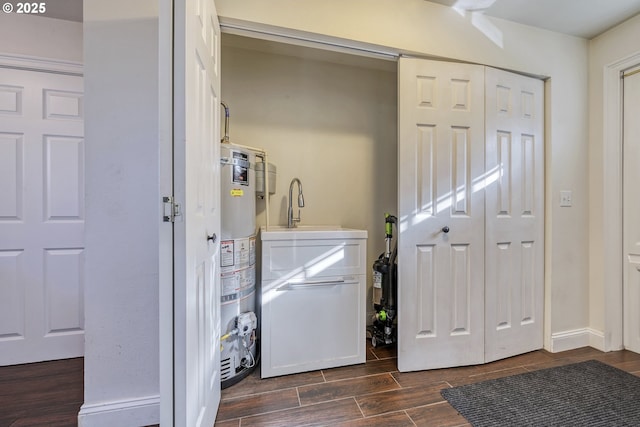 laundry room featuring gas water heater, laundry area, a sink, baseboards, and wood tiled floor