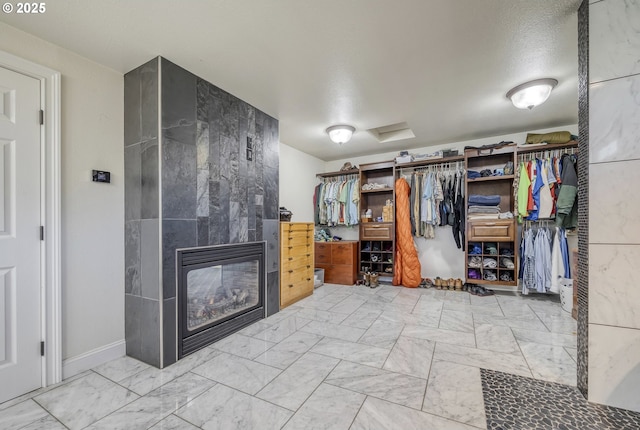 spacious closet with marble finish floor, a tile fireplace, and attic access