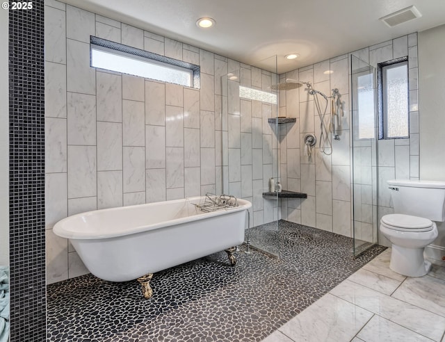 full bathroom with marble finish floor, tile walls, toilet, a freestanding tub, and walk in shower