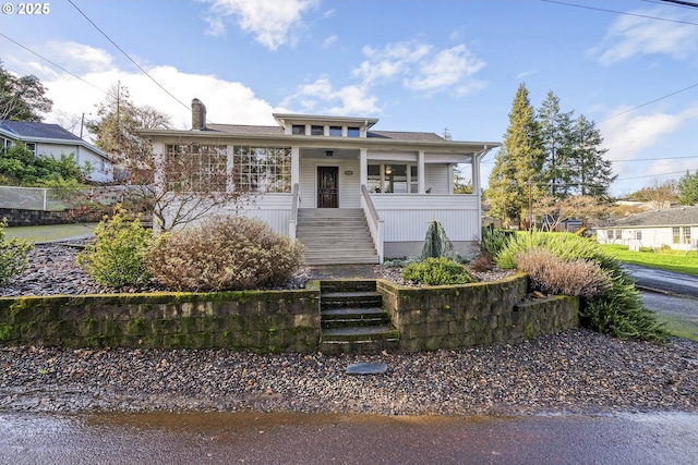 view of front of home featuring a chimney, covered porch, and stairway