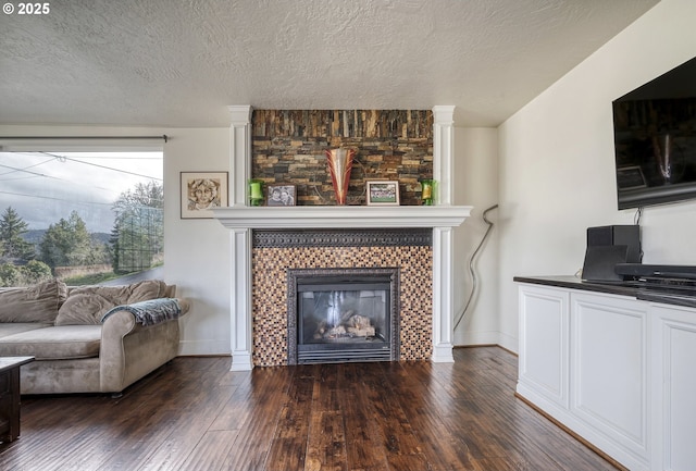 living room featuring a textured ceiling, baseboards, dark wood-type flooring, and a tile fireplace