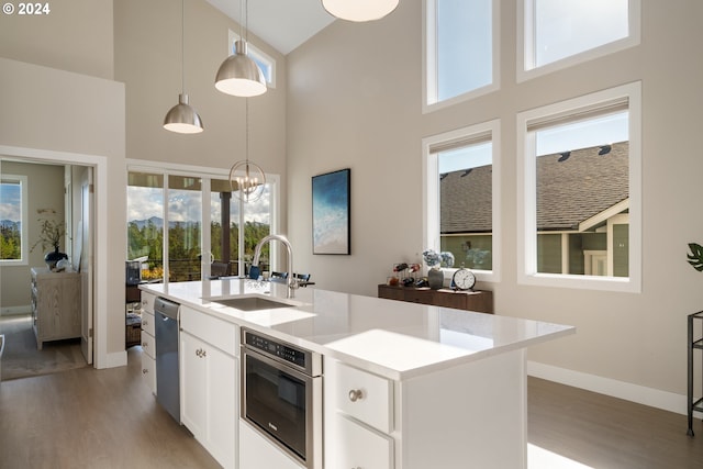 kitchen with a high ceiling, white cabinets, hanging light fixtures, and an island with sink